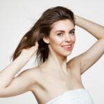 beautiful young woman with perfect clean skin smiling touching hair white wall facial treatment