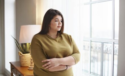 people lifestyle body positivity concept beautiful young brunette female with extra pounds standing by window home crossing arms her chest having thoughtful pensive look pondering