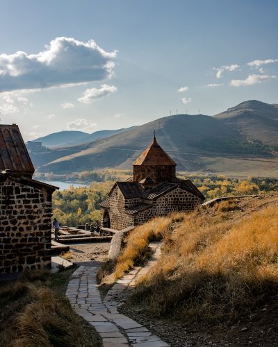brown concrete house on green grass field near mountain under white clouds during daytime
